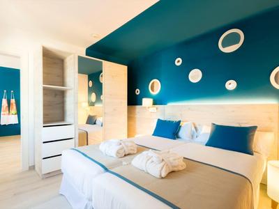 Modernes Schlafzimmer mit großem Bett, blauer Wand, Spiegeln und heller Holzmöblierung.