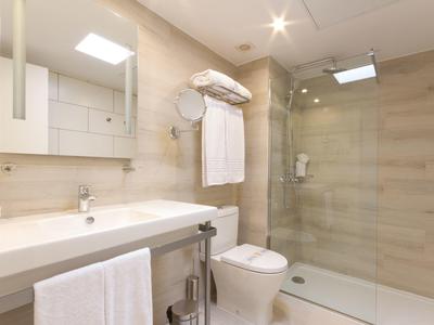 Helles Bad mit weißem Waschbecken, WC, Duschkabine und großen Wandfliesen in Beige.