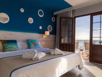 Modernes Schlafzimmer mit Doppelbett, blauer Wand, Holzakzent und Balkon mit Meerblick.