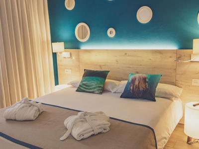 Hotelzimmer mit Doppelbett, blauer Wand, hölzernem Kopfteil, dekorativen Tellern und weichen Bademänteln.