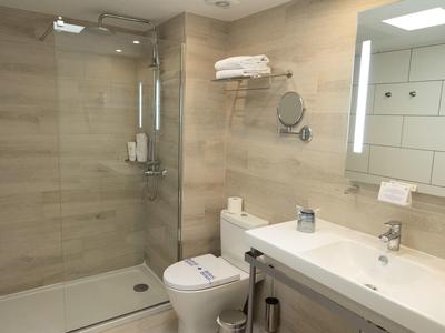Helles, modernes Badezimmer mit großer Dusche, Toilette, Waschbecken und Wandspiegel mit Beleuchtung.