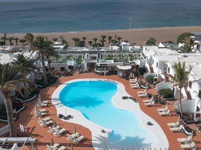 Großer, geschwungener Pool mit Liegestühlen, Palmen und Meer im Hintergrund an einem Hotelstrand.