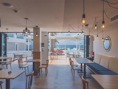 Modernes, helles Café mit Holzböden, einfachen Tischen und Stühlen, offenen Glastüren und Meerblick.