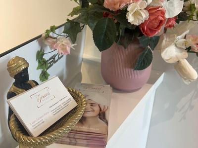 Arrangement aus rosa und weißen Blumen in Vase, daneben goldene Büste mit Kartenhalter auf weißem Podest.