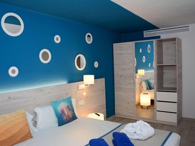 Schlafzimmer mit blauer Wand, rundem Dekor, großem Spiegelkleiderschrank und Doppelbett mit Kissen.
