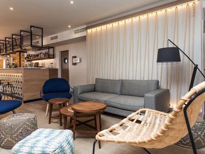 Modernes Wohnzimmer mit grauem Sofa, blauen Sesseln, Holz- und Metallmöbeln sowie indirekter Beleuchtung.