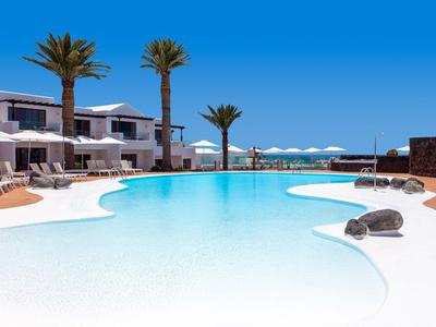 Piscine moderne d'hôtel avec transats et palmiers sous un ciel bleu au bord de la mer.