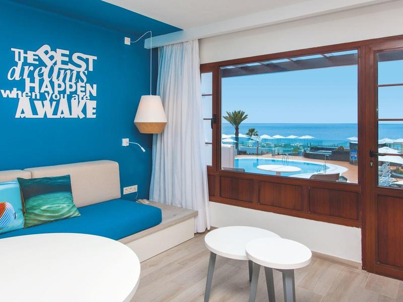 Camera d'hotel moderna con terrazza e vista mare, angolo salotto accogliente con divano blu.