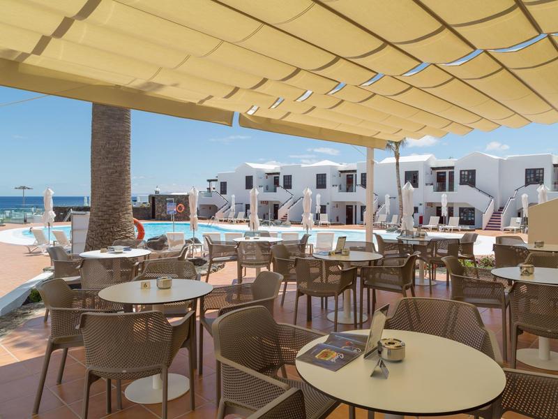 Terrazza di un caffè con tavoli e sedie sotto tende da sole sulla costa.