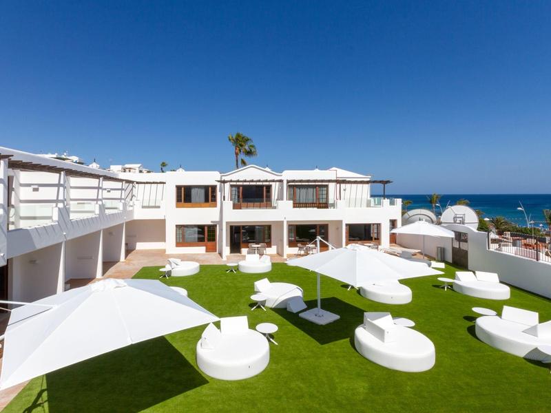 Giardino moderno dell'hotel con mobili bianchi e vista sul mare sotto un cielo limpido.