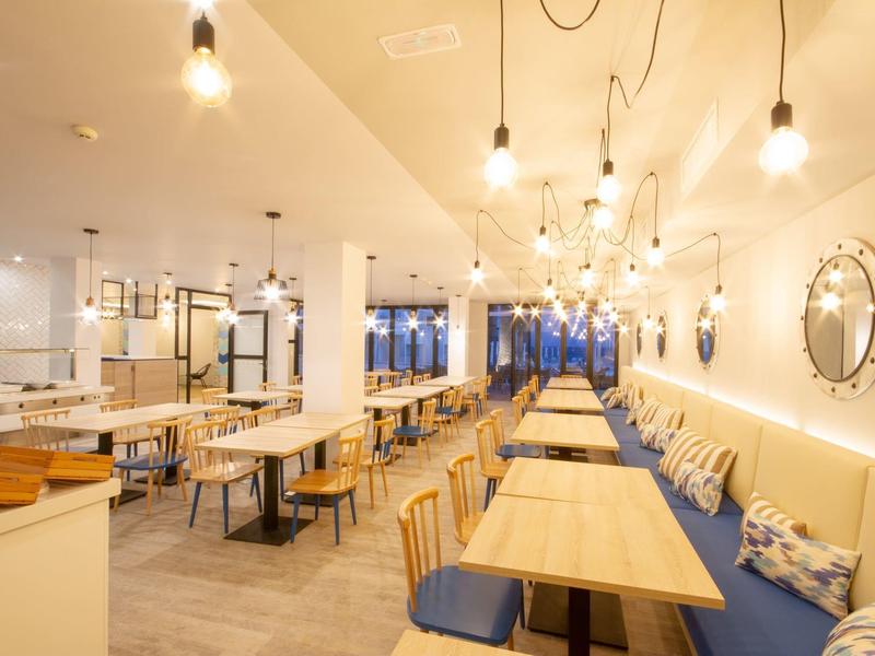 Interno di un hotel moderno con tavoli, sedie e illuminazione calda.