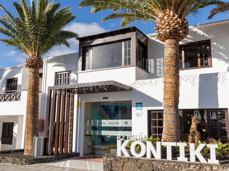 Hotel moderno con facciata bianca, grandi finestre e palme all'ingresso.