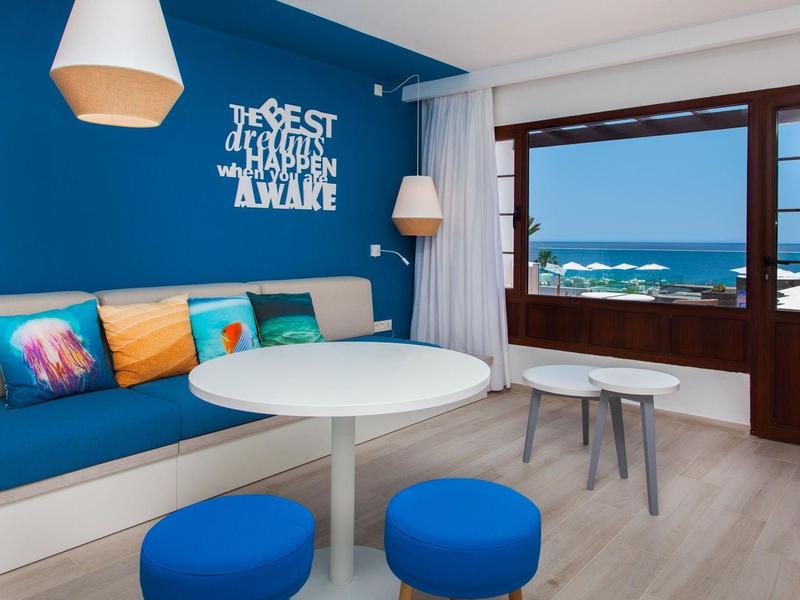 Camera d'hotel moderna con sedute blu e vista mare dal balcone.