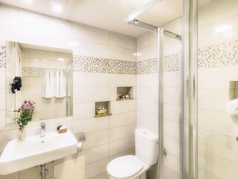 Bagno luminoso con doccia, wc, lavabo e specchio con mensole alle pareti.