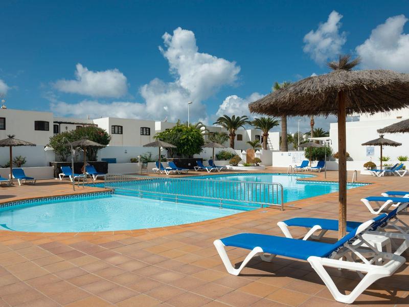 Piscina dell'hotel con sdraio e ombrelloni di paglia sotto un cielo azzurro.