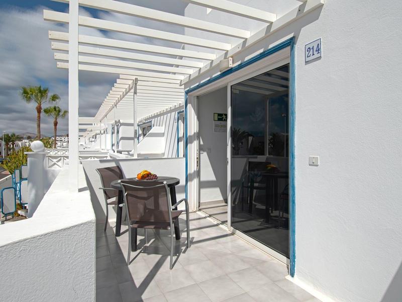 Balcone con due sedie, tavolo e porta a vetri aperta su edificio bianco con sole.