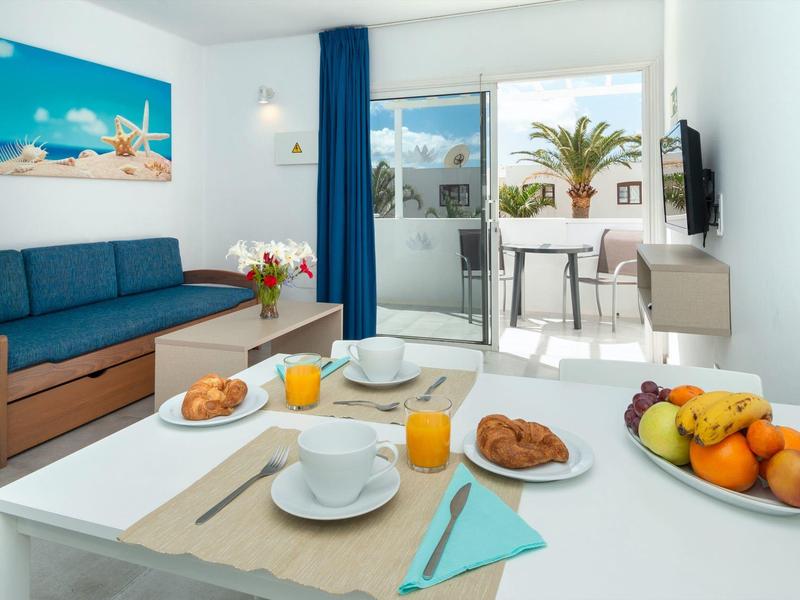 Soggiorno luminoso con divano blu, tavolo da pranzo e terrazza con vista su una palma.