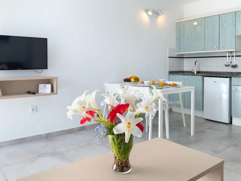 Cucina moderna e luminosa con TV, tavolo da pranzo e composizione floreale sul tavolo.