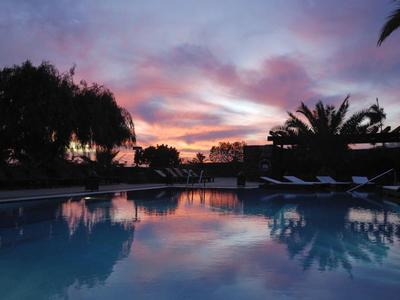 Basen o zachodzie słońca z kolorowym niebem i palmami w tle.