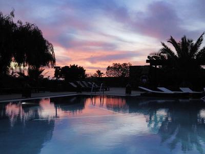 Ein ruhiger Pool spiegelt den bunten Abendhimmel mit Wolken und Silhouetten von Bäumen.