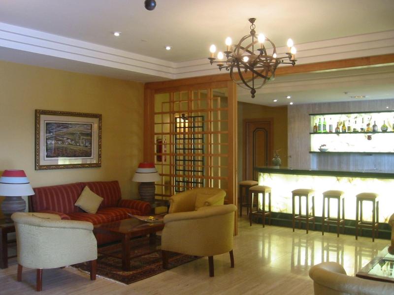 Przytulna część hotelowego lobby z sofami, fotelami i podświetlonym barem w tle.