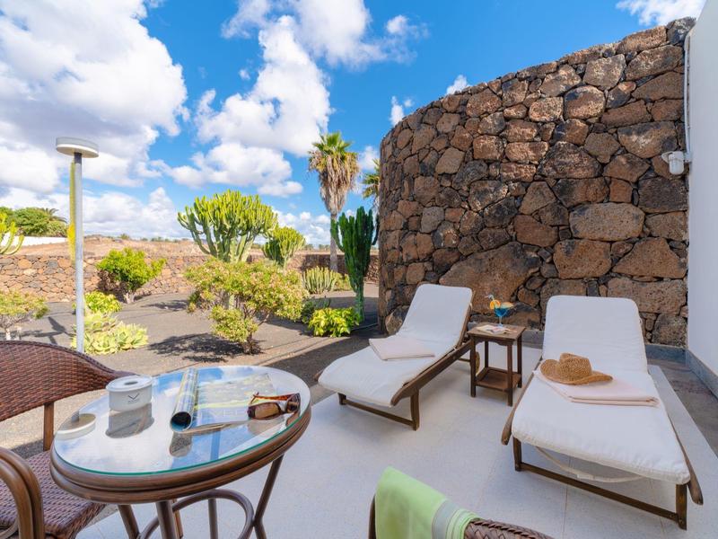 Taras z leżakami, stołem i krzesłami przy kamiennym murze w słonecznym ogrodzie.