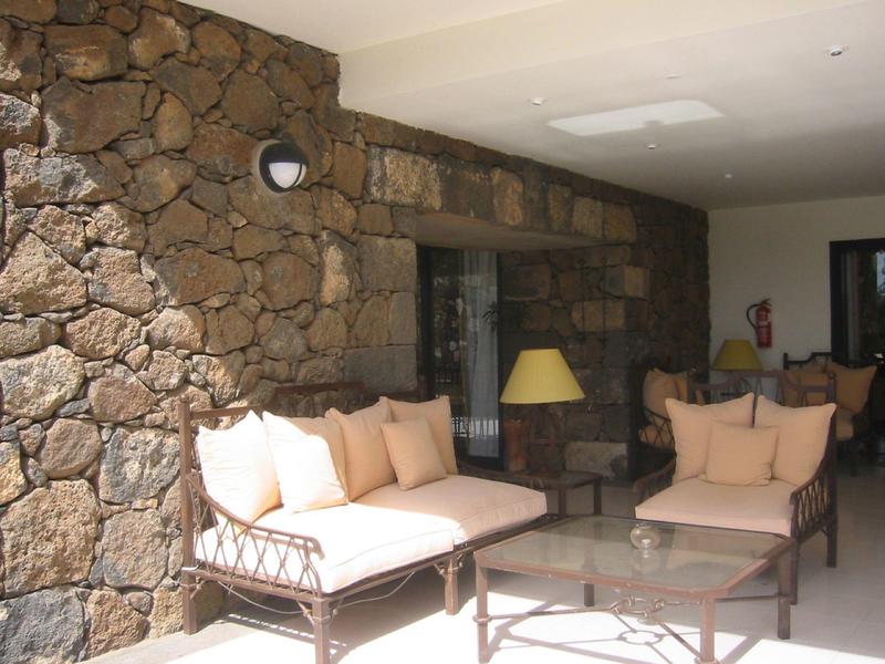 Przytulny kącik wypoczynkowy z tapicerowanymi meblami i lampą przy kamiennej ścianie w hotelu.