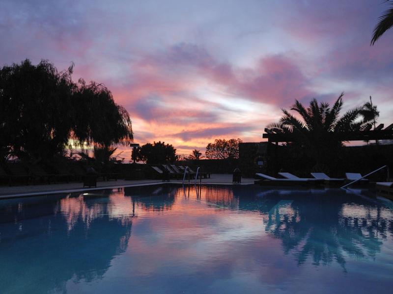 Basen o zachodzie słońca z kolorowym niebem i palmami w tle.