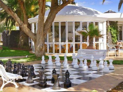 Grande scacchiera nell'area giardino di un hotel con panchine e ombrelloni.