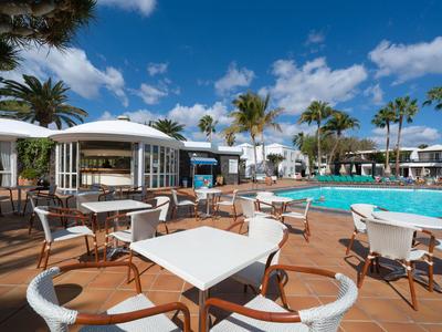 Terrazza dell'hotel con tavoli e sedie accanto a una piscina sotto un cielo blu.