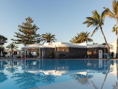 Area piscina moderna con bar e palme sotto un cielo limpido in un resort per vacanze.