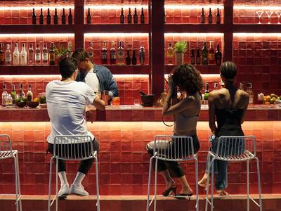 Tre persone sedute al bar con scaffali illuminati di rosso che parlano con il barista.