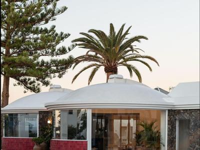 Bungalow moderno con piscina y palmeras al fondo bajo un cielo despejado.