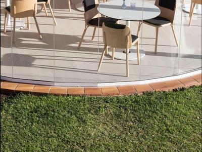Área exterior de restaurante con mesas blancas redondas y sillas de madera en una terraza junto al césped