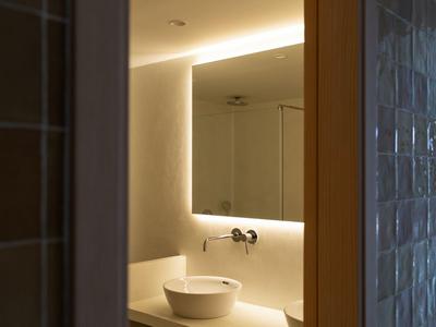 Bagno moderno con lavabo rotondo e illuminazione indiretta dietro lo specchio.