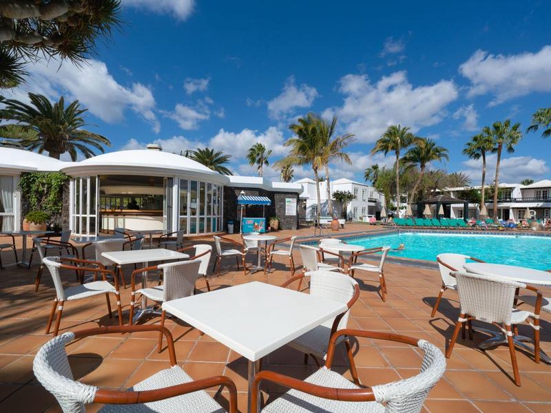 Terrazza dell'hotel con tavoli e sedie accanto a una piscina sotto un cielo blu.