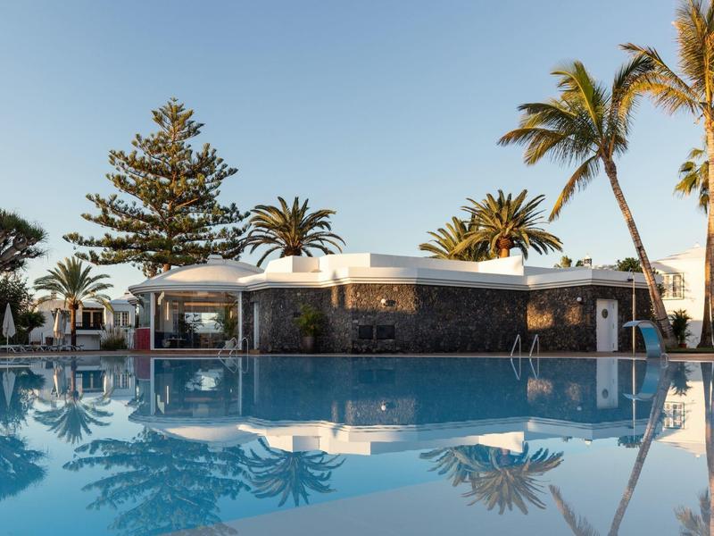 Area piscina moderna con bar e palme sotto un cielo limpido in un resort per vacanze.