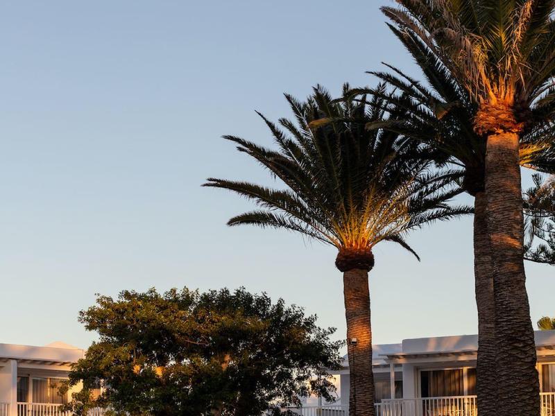 Complesso alberghiero moderno con palme e ombrelloni sotto un cielo limpido.