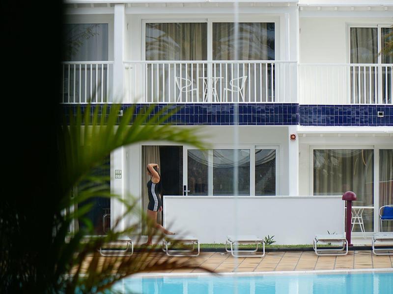 Vista di un hotel con piscina in primo piano e una persona all'ingresso.