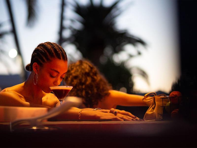 Donna si rilassa la sera in una vasca idromassaggio con bevanda in mano sotto le palme.