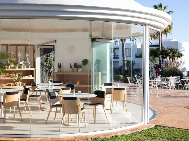 Facciata curva in vetro di un caffè moderno con tavoli e sedie su una terrazza.