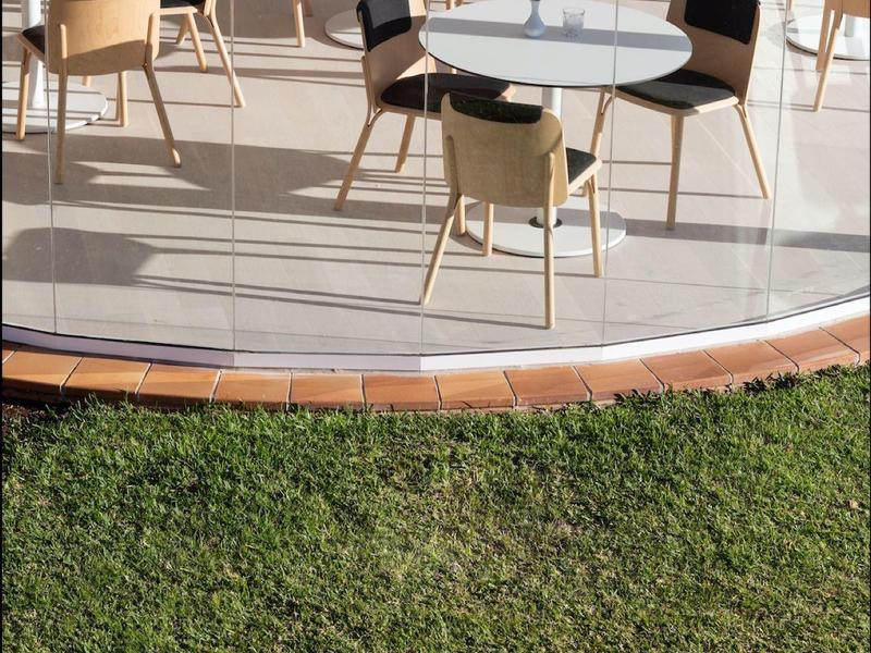 Area esterna moderna con tavoli e sedie su una terrazza accanto a un prato