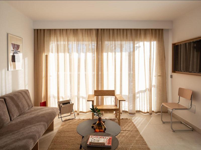 Soggiorno luminoso con divano, sedie, tappeto e grandi finestre con tende.