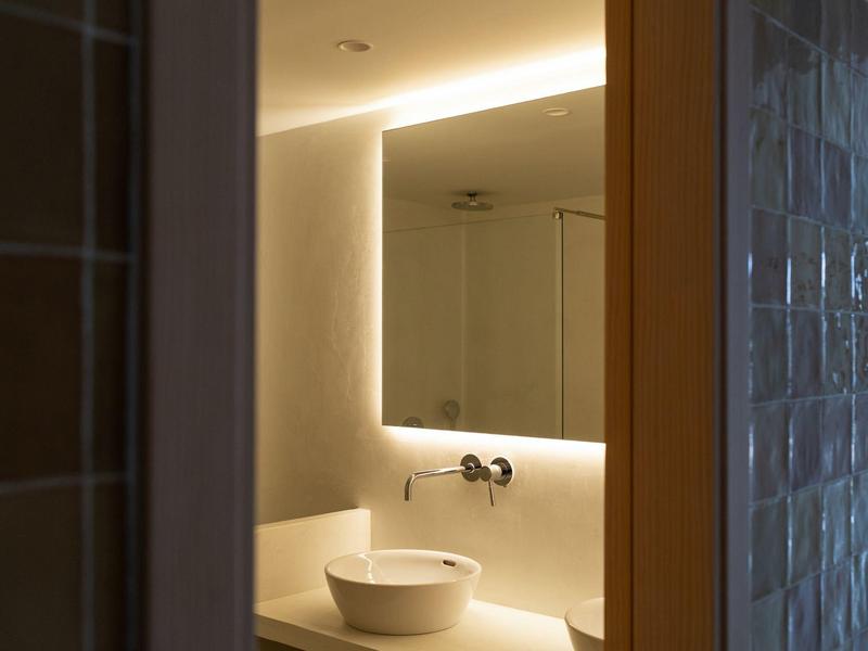 Bagno moderno con lavabo rotondo e illuminazione indiretta dietro lo specchio.