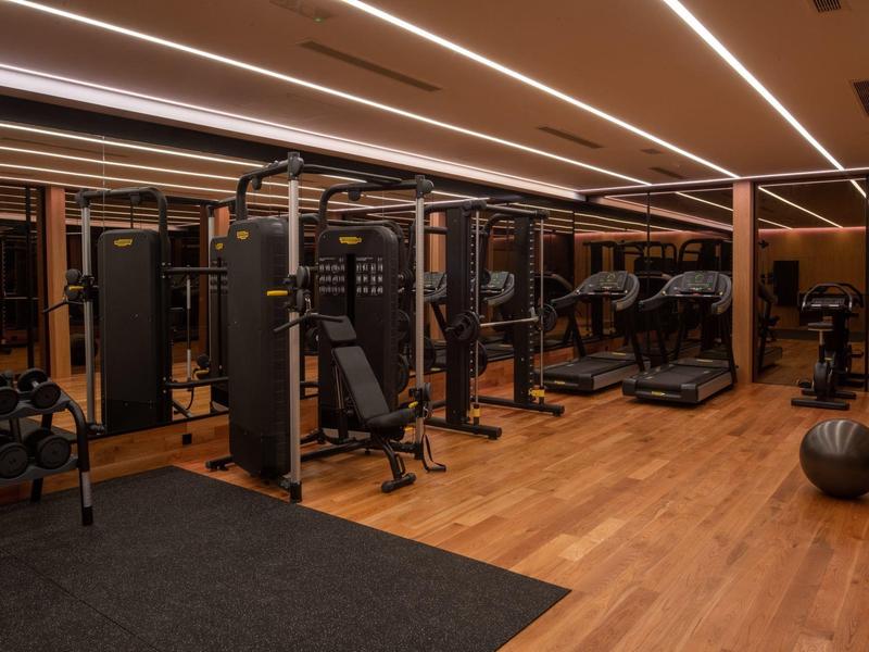 Palestra moderna con pavimento in legno, attrezzature per allenamento e specchi in un hotel.