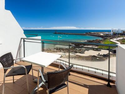 Balkon mit zwei Stühlen und Tisch, Blick auf Meer, Strand und bewölkten Himmel.