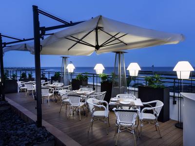 Moderne Außenterrasse mit weißen Stühlen, Tischen, großen Sonnenschirmen und Lampen bei Dämmerung.