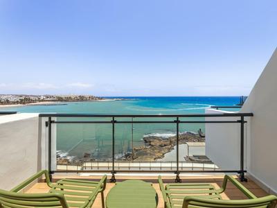 Balkon mit grünen Stühlen und Tisch, Glasgeländer, Blick auf Meer und klare blaue Himmel.