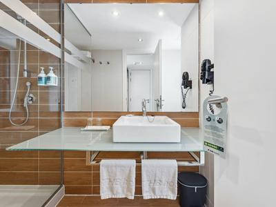 Modernes Bad mit rechteckigem Waschbecken, Glasablage, braunen Fliesen und großer Spiegelwand.