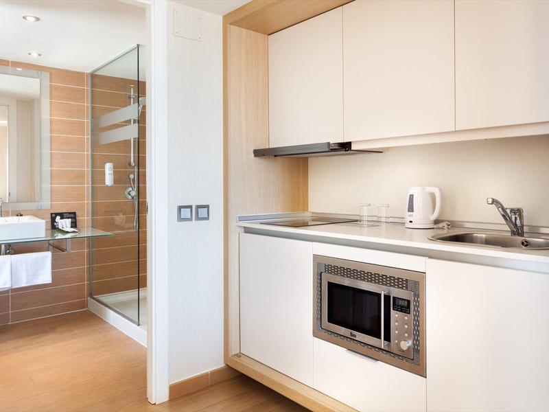 Angolo cottura compatto con microonde, bollitore e lavandino in una camera d'hotel moderna.